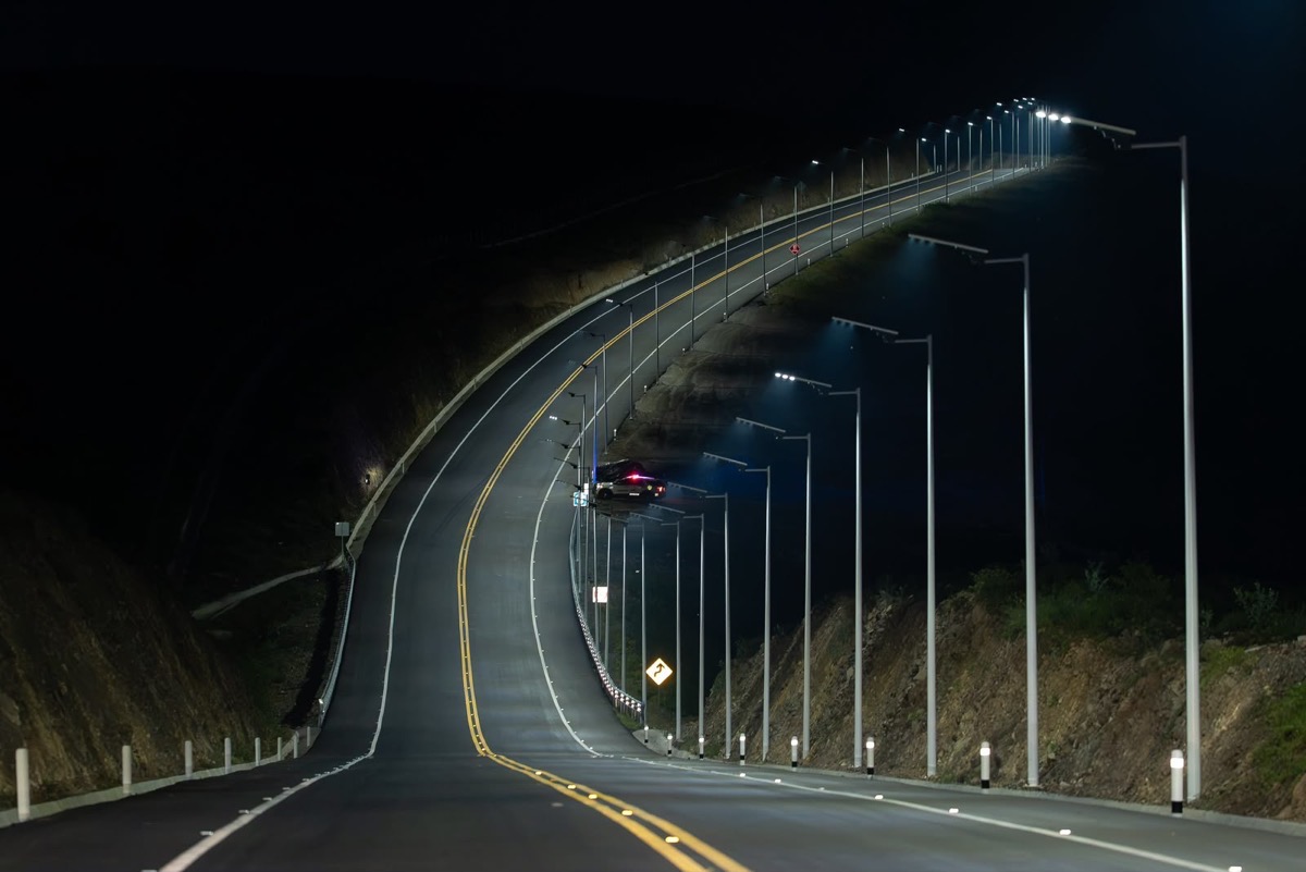 Una carretera iluminada por farolas se curva y sube por una colina durante la noche.