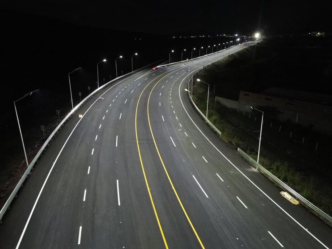 Carretera nocturna con iluminación de faroles a lo largo de una curva amplia, líneas amarillas centrales y marcas blancas en弘.