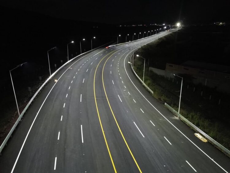 Carretera nocturna con iluminación de faroles a lo largo de una curva amplia, líneas amarillas centrales y marcas blancas en弘.