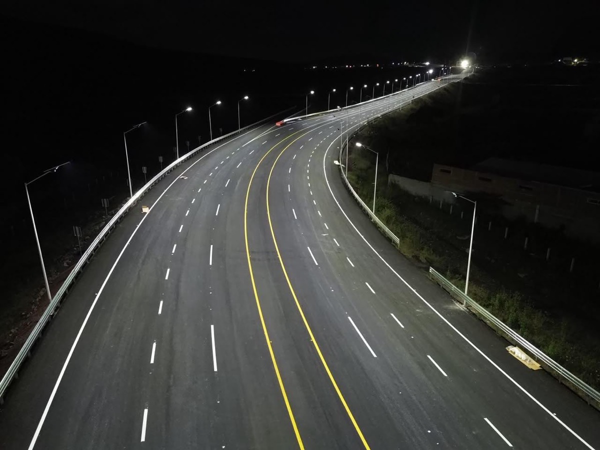 Carretera nocturna con iluminación de faroles a lo largo de una curva amplia, líneas amarillas centrales y marcas blancas en弘.