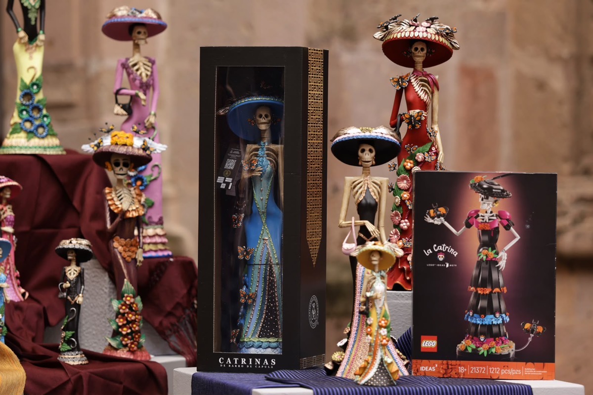 Varias figuras de calaveras vestidas con trajes coloridos y sombreros están exhibidas junto a una caja y un set de LEGO inspirado en una de ellas.