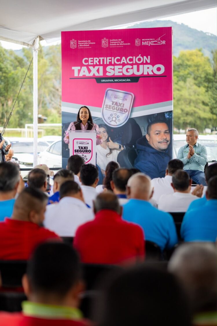 Una mujer habla en un podio frente a un grupo de personas durante un evento de certificación de taxis seguros en Uruapan, Michoacán.
