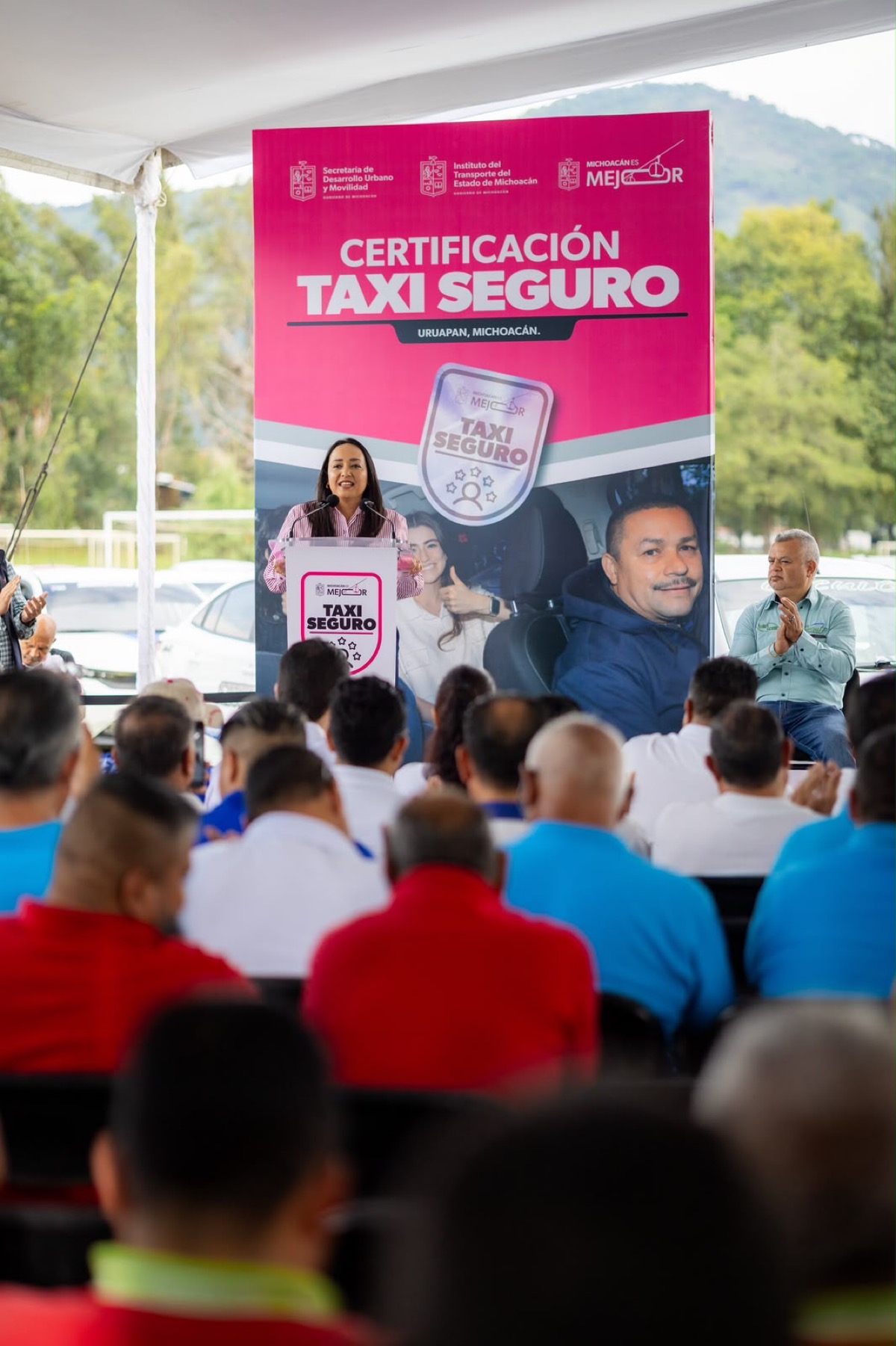 Una mujer habla en un podio frente a un grupo de personas durante un evento de certificación de taxis seguros en Uruapan, Michoacán.