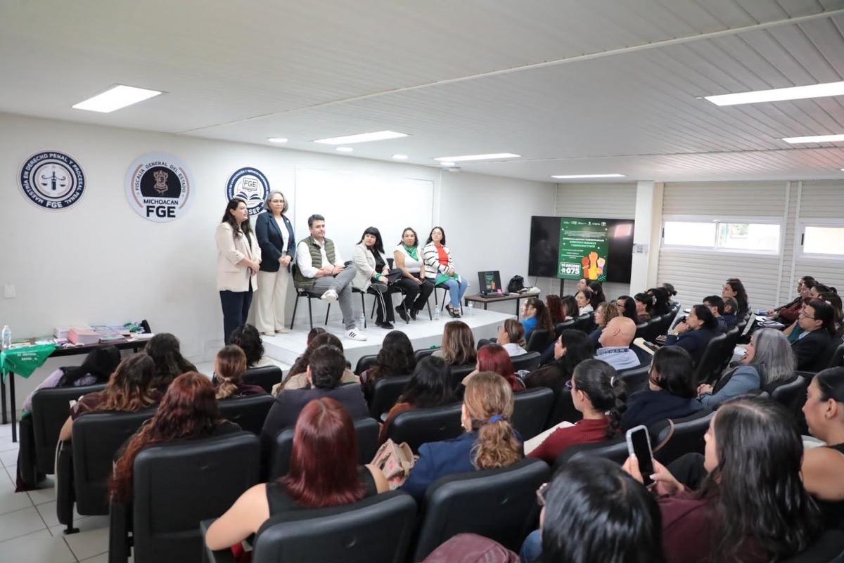 Un grupo de personas está sentado en un auditorio mientras varias personas presentan en un escenario al frente de la sala.