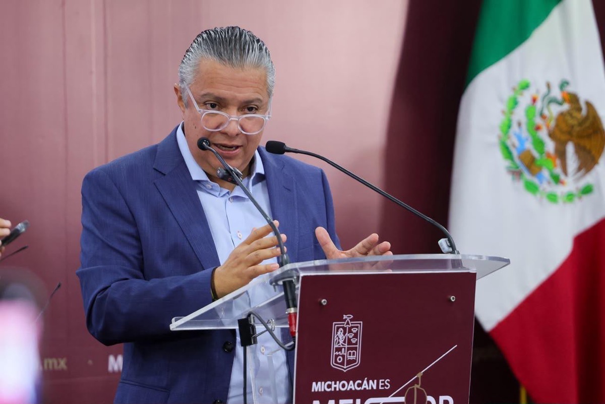 Un hombre de traje azul habla en un podio con micrófonos frente a una bandera de México.