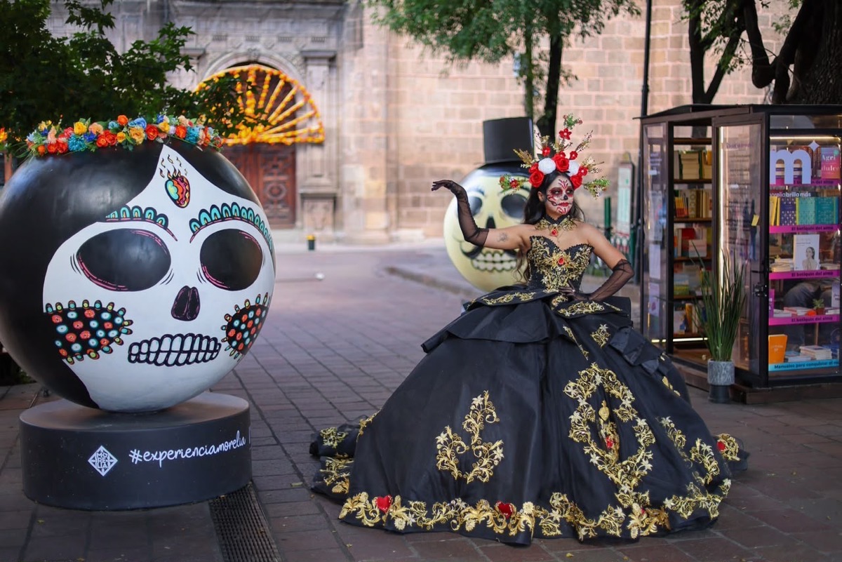 Catrina con vestido negro posa entre calaveras decoradas en el Centro Histórico de Morelia durante Día de Muertos.