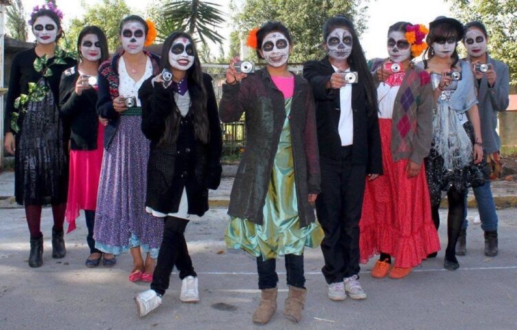 Un grupo de personas con la cara pintada de calaveras posa para la cámara, varias sosteniendo cámaras fotográficas.
