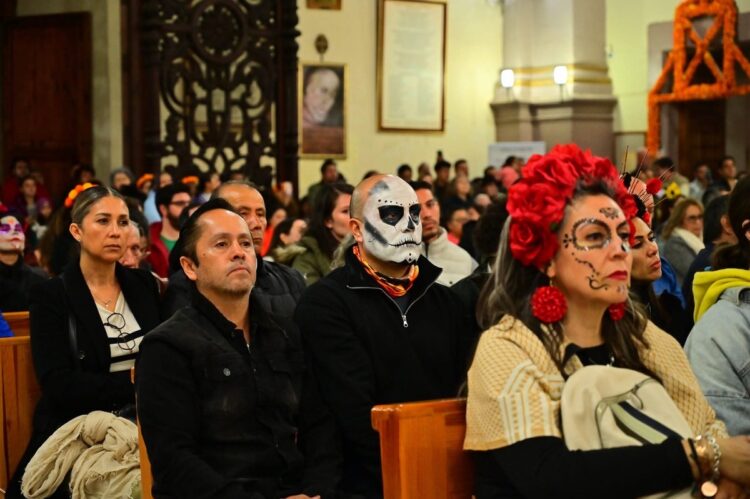 Asistentes en un evento cultural con máscaras, maquillaje y trajes tradicionales, en un recinto con decoraciones y personas a.
