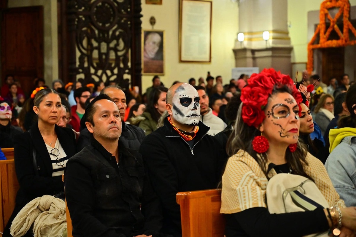 Asistentes en un evento cultural con máscaras, maquillaje y trajes tradicionales, en un recinto con decoraciones y personas a.