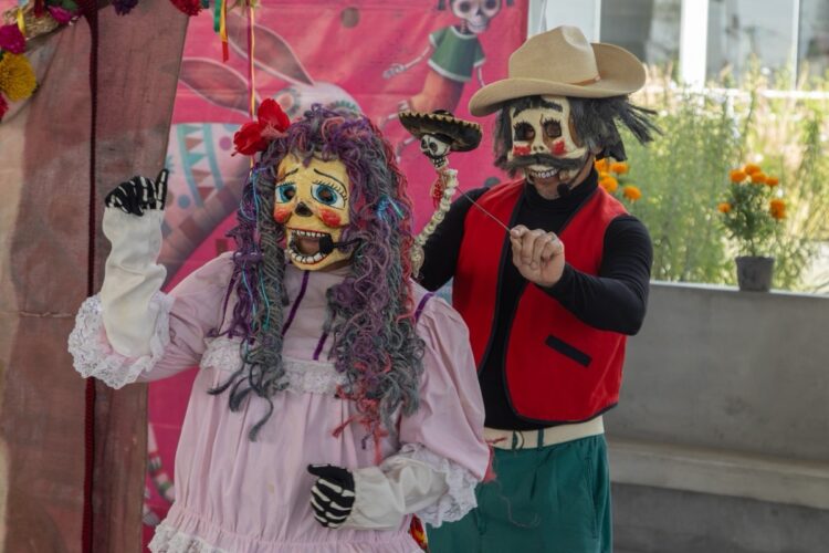 Dos personas con disfraces y máscaras de calaveras coloridas participan en una presentación festiva.