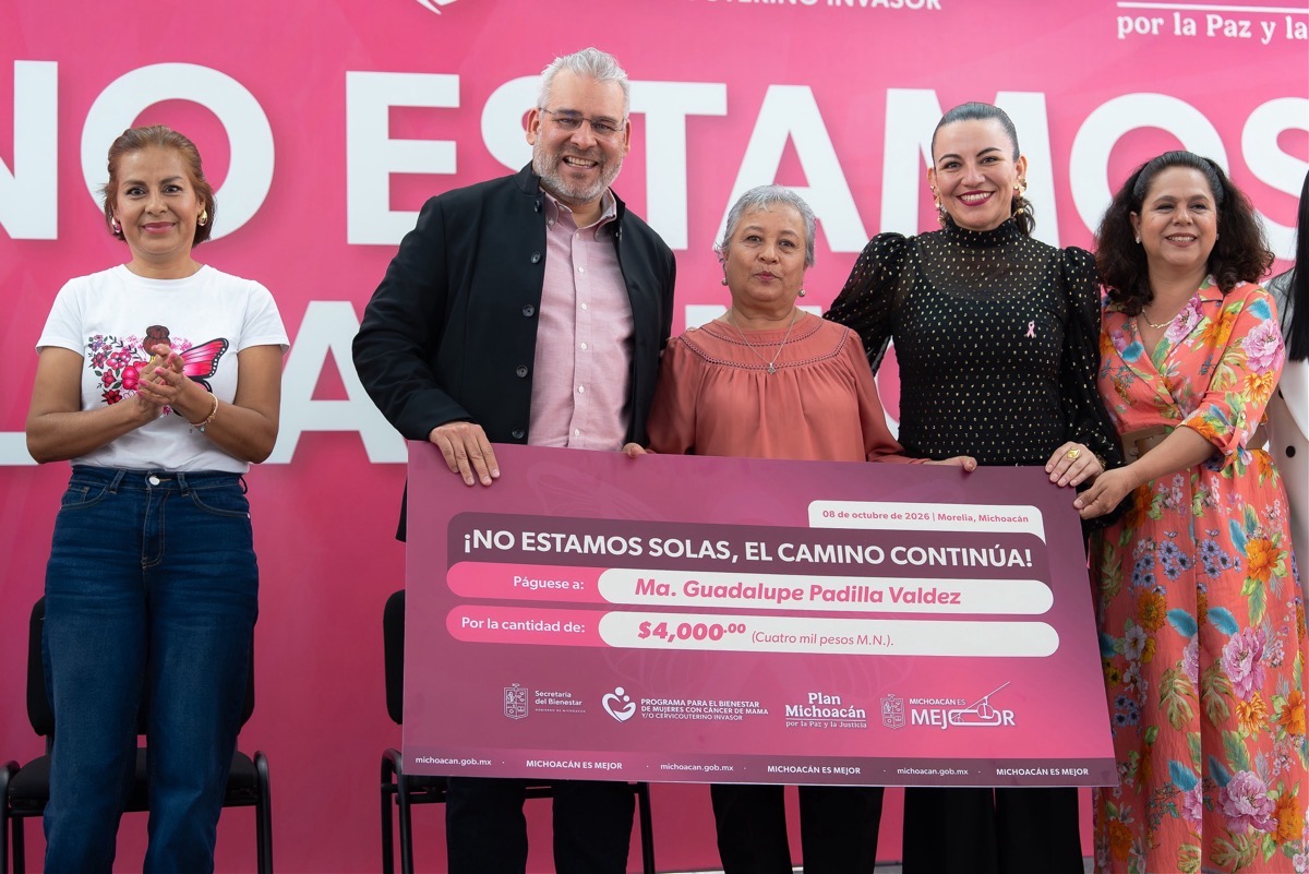 Cinco personas posan sonriendo mientras una de ellas sostiene un cheque grande rosa en un evento público.