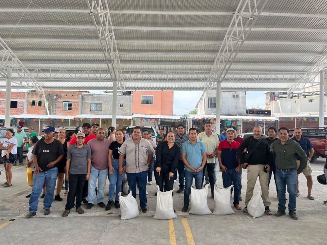 Un grupo de personas posa de pie bajo un techo grande, con varias bolsas blancas en el suelo frente a ellas.