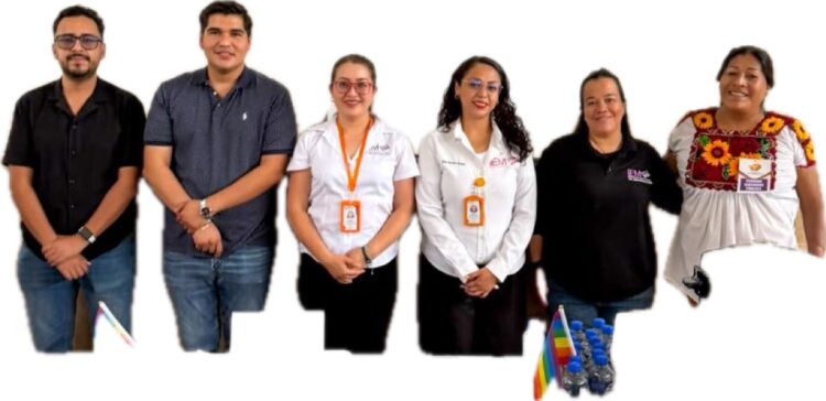 Seis personas posan de pie en fila, algunas con uniformes y gafetes, junto a unas botellas de agua y pequeñas banderas de colores.
