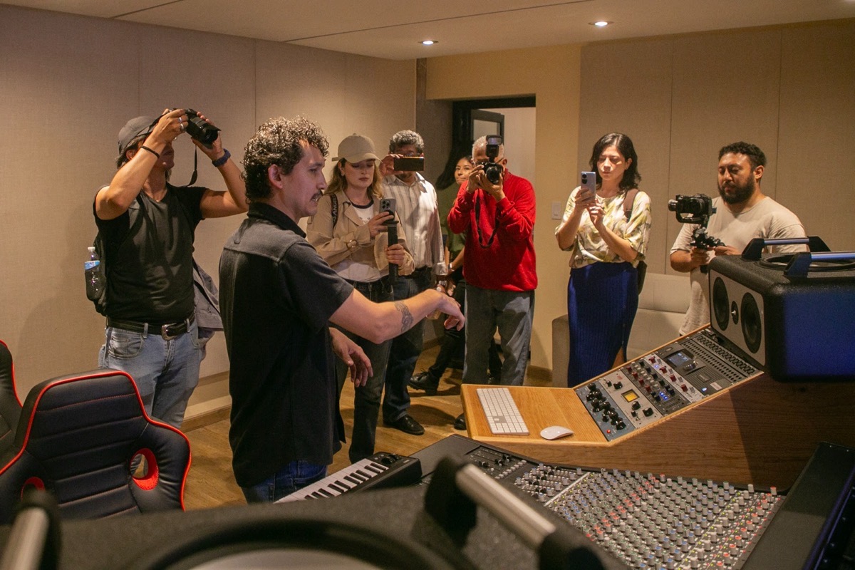 Un grupo de personas toma fotos y graba en un estudio de grabación mientras un hombre señala el equipo de audio.