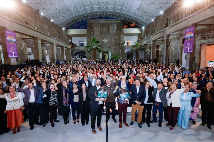 Un gran grupo de personas posa juntas en el interior de un edificio amplio con techo de cristal y muros de piedra.