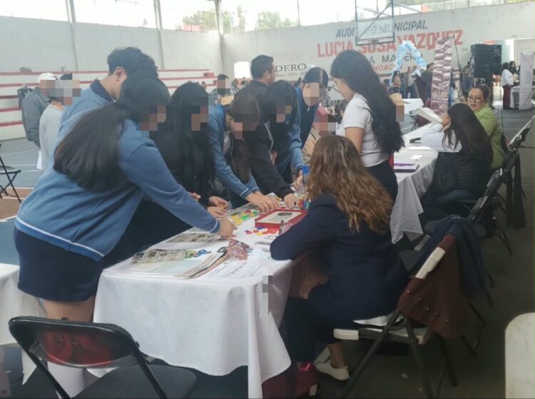 Un grupo de personas, en su mayoría jóvenes, participa en actividades de mesa dentro de un gimnasio cubierto.