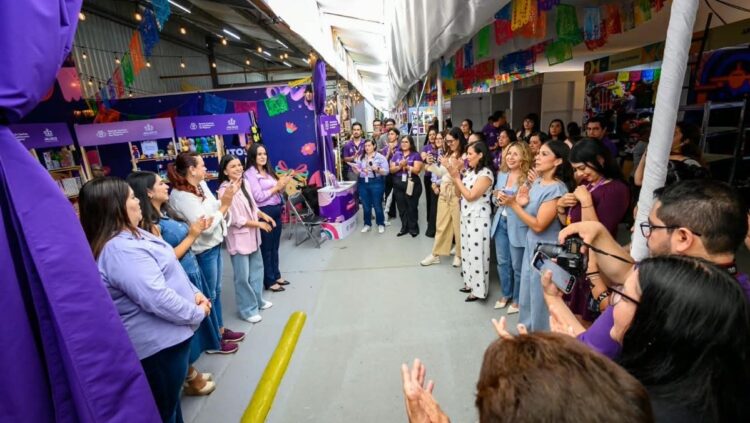 Un grupo de personas se encuentra en un pasillo decorado, formando un círculo y aplaudiendo mientras algunas toman fotos.