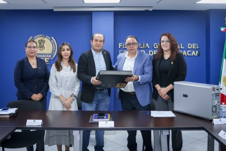 Cinco personas posan en una sala de conferencias, mientras dos de ellas sostienen una computadora frente a una mesa con documentos y equipo electrónico.