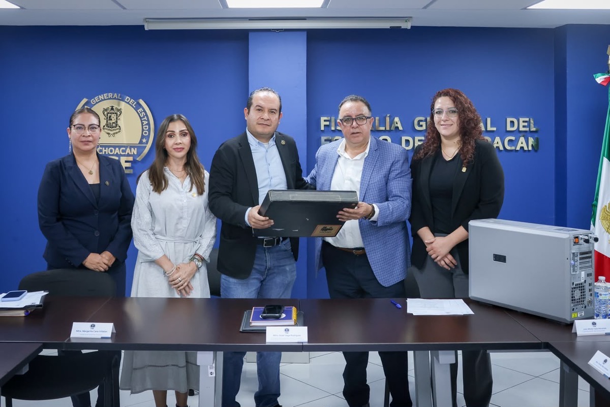 Cinco personas posan en una sala de conferencias, mientras dos de ellas sostienen una computadora frente a una mesa con documentos y equipo electrónico.