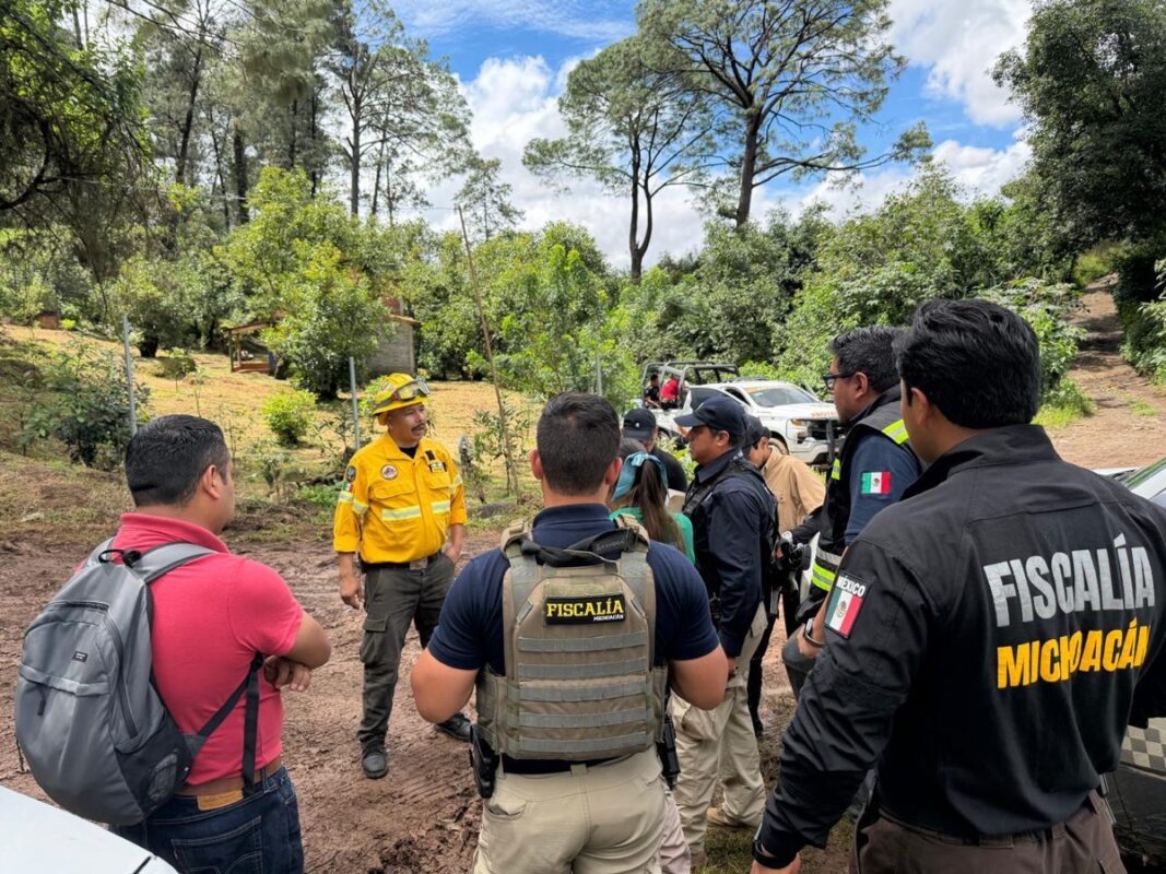 Un grupo de personas, incluyendo oficiales de la Fiscalía de Michoacán y un hombre con uniforme amarillo, conversa al aire libre en una zona boscosa.