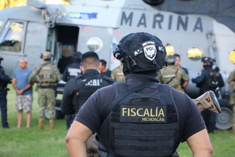 Agentes de la Fiscalía de Michoacán y Marina custodian detenidos frente a un helicóptero militar.