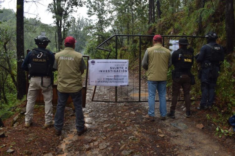 Seis personas, incluyendo agentes de la fiscalía y oficiales, están frente a un portón en un bosque con un cartel que indica que el lugar está bajo investigación.