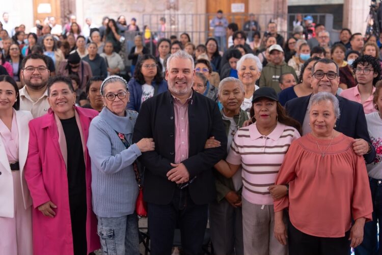 Un grupo de personas sonríe y posa para una foto en un evento con más gente al fondo.