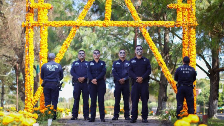 Policías de la Guardia Civil con rostros pintados vigilan un arco de cempasúchil en Michoacán
