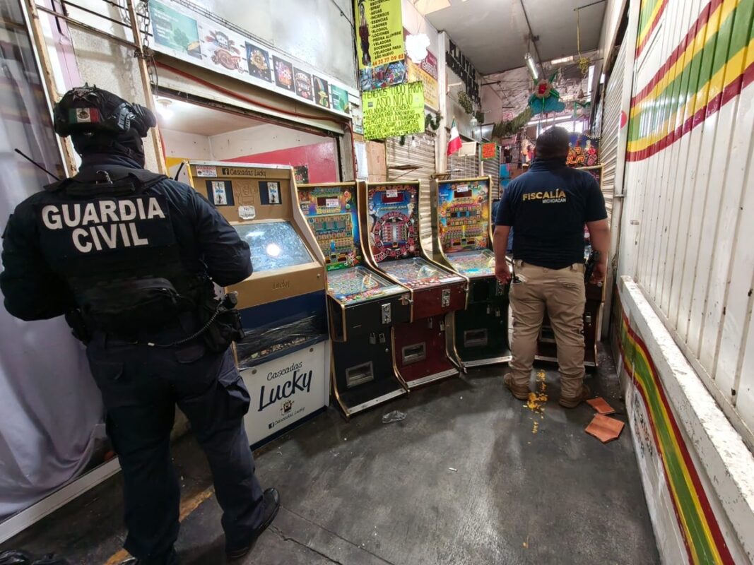 Dos oficiales, uno de la Guardia Civil y otro de la Fiscalía, inspeccionan máquinas tragamonedas en un pasillo estrecho.