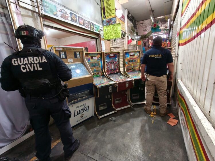 Dos oficiales, uno de la Guardia Civil y otro de la Fiscalía, inspeccionan máquinas tragamonedas en un pasillo estrecho.