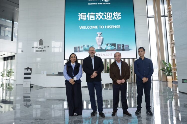 Cuatro personas posan para una foto en el vestíbulo de un edificio moderno frente a una pantalla que dice “Welcome to Hisense”.