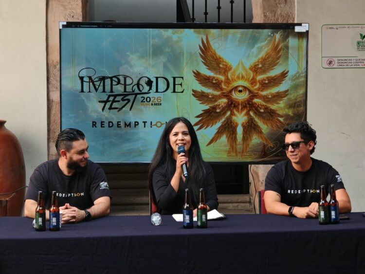 Tres personas sentadas en una mesa con botellas de cerveza hablan frente a un cartel que anuncia un festival llamado Implode Fest 2026.