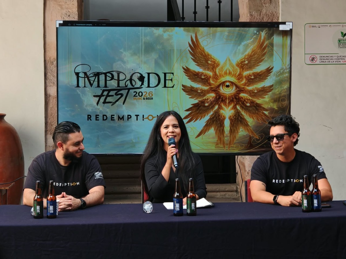 Tres personas sentadas en una mesa con botellas de cerveza hablan frente a un cartel que anuncia un festival llamado Implode Fest 2026.
