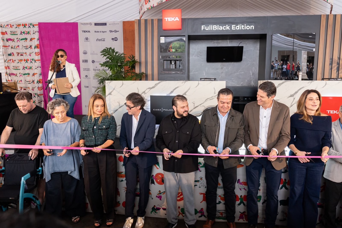 Un grupo de personas está cortando una cinta rosa en una ceremonia de inauguración mientras una mujer habla en un podio al fondo.