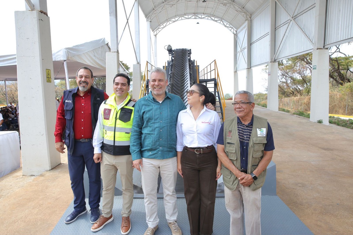 Cinco personas posan sonrientes frente a una estructura metálica y un equipo industrial en un espacio techado al aire libre.