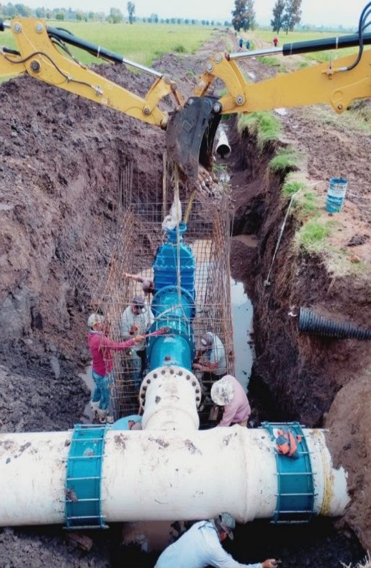 Trabajadores instalan tubería de riego con excavadora en Michoacán