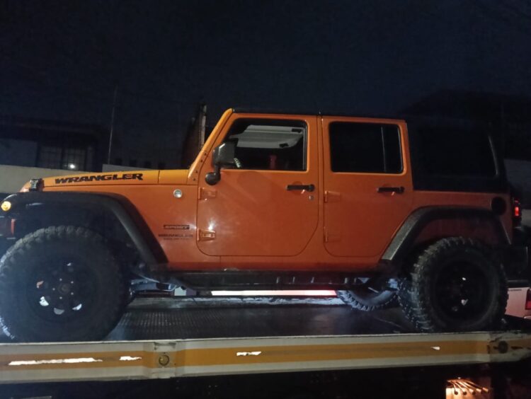 Un Jeep Wrangler naranja está sobre una plataforma de remolque durante la noche.