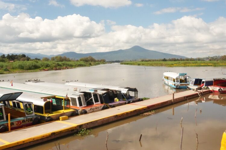 Botes atracados en el muelle del lago de Pátzcuaro con montañas al fondo en temporada de Noche de Muertos