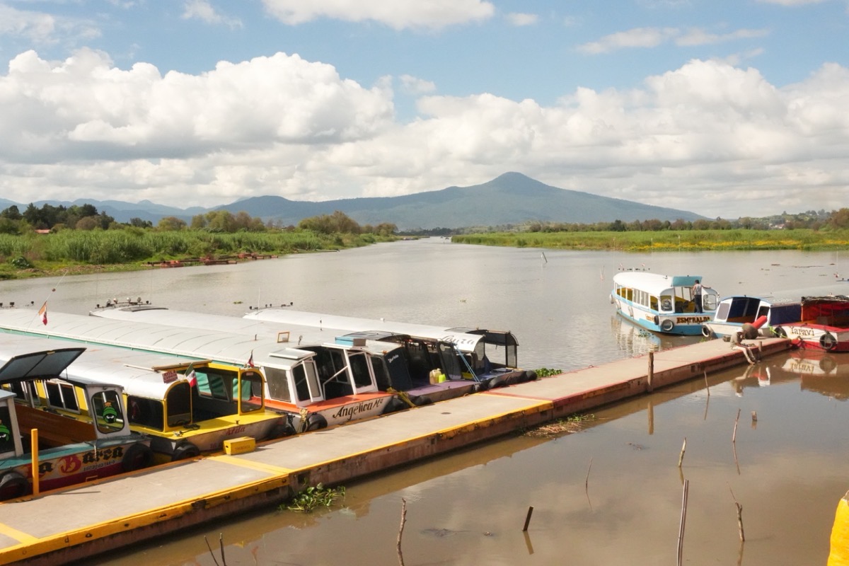 Botes atracados en el muelle del lago de Pátzcuaro con montañas al fondo en temporada de Noche de Muertos