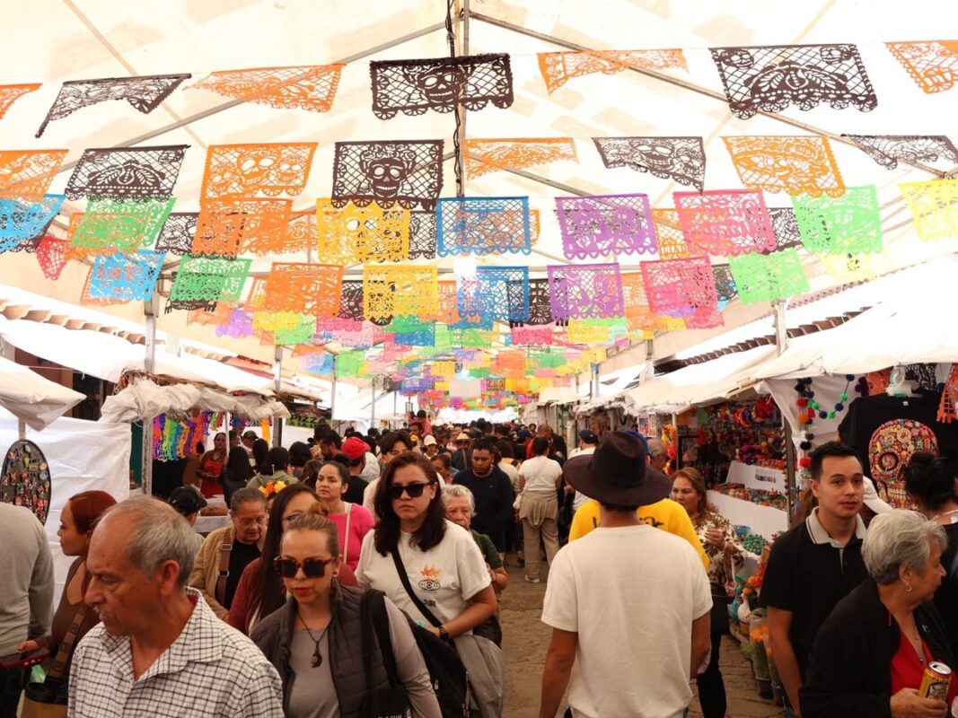 Visitantes recorren la Feria de la Catrina en Capula bajo coloridos banderines de papel picado.