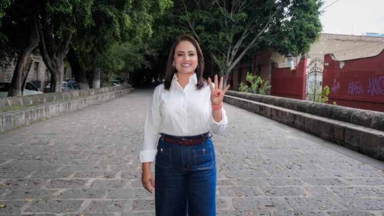 Una mujer de pie en una calle empedrada al aire libre levanta una mano mostrando cuatro dedos.