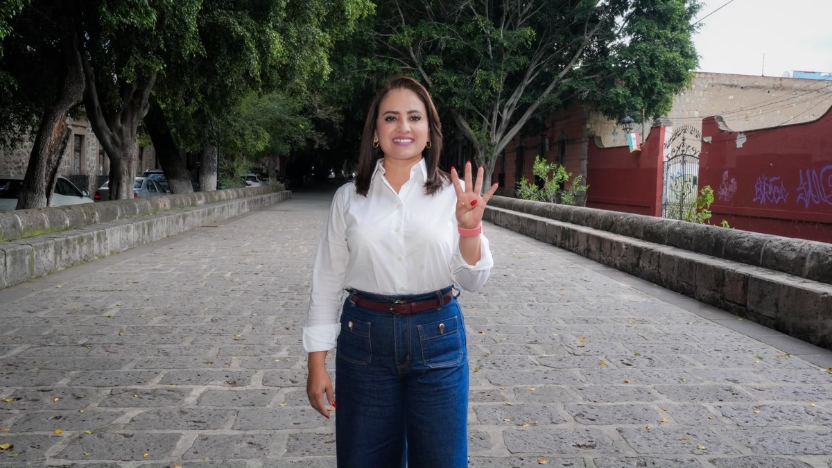 Una mujer de pie en una calle empedrada al aire libre levanta una mano mostrando cuatro dedos.