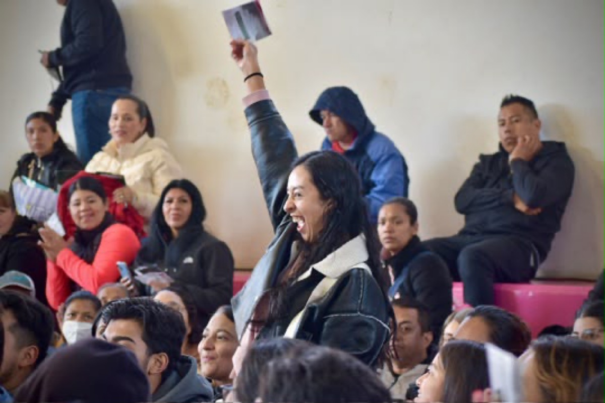 Mujer celebra con un papel en alto durante el sorteo de viviendas en Pátzcuaro.
