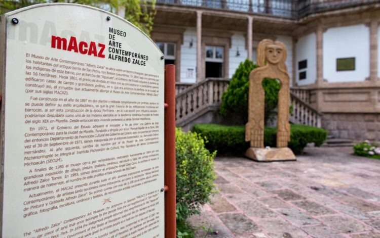 Un cartel informativo del Museo de Arte Contemporáneo Alfredo Zalce se encuentra frente a un edificio histórico con una escultura en el jardín.