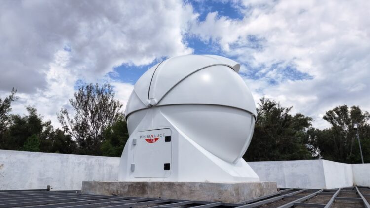 Un observatorio esférico blanco con cielo parcialmente nublado y árboles de fondo.