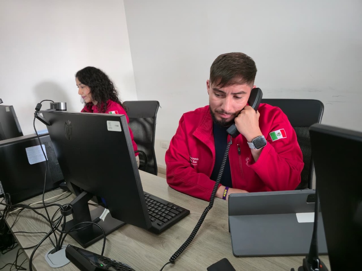 Dos personas con chaquetas rojas trabajan en escritorios con computadoras, una usando un teléfono y la otra escribiendo.