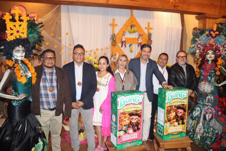Un grupo de personas posa sonriente frente a un altar decorado con flores y figuras de catrinas coloridas.