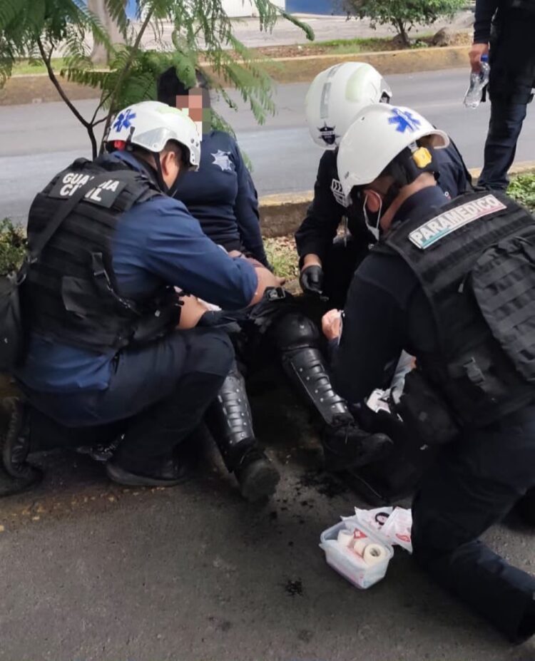 Paramédicos atienden a un oficial herido en la acera mientras otros policías lo rodean.