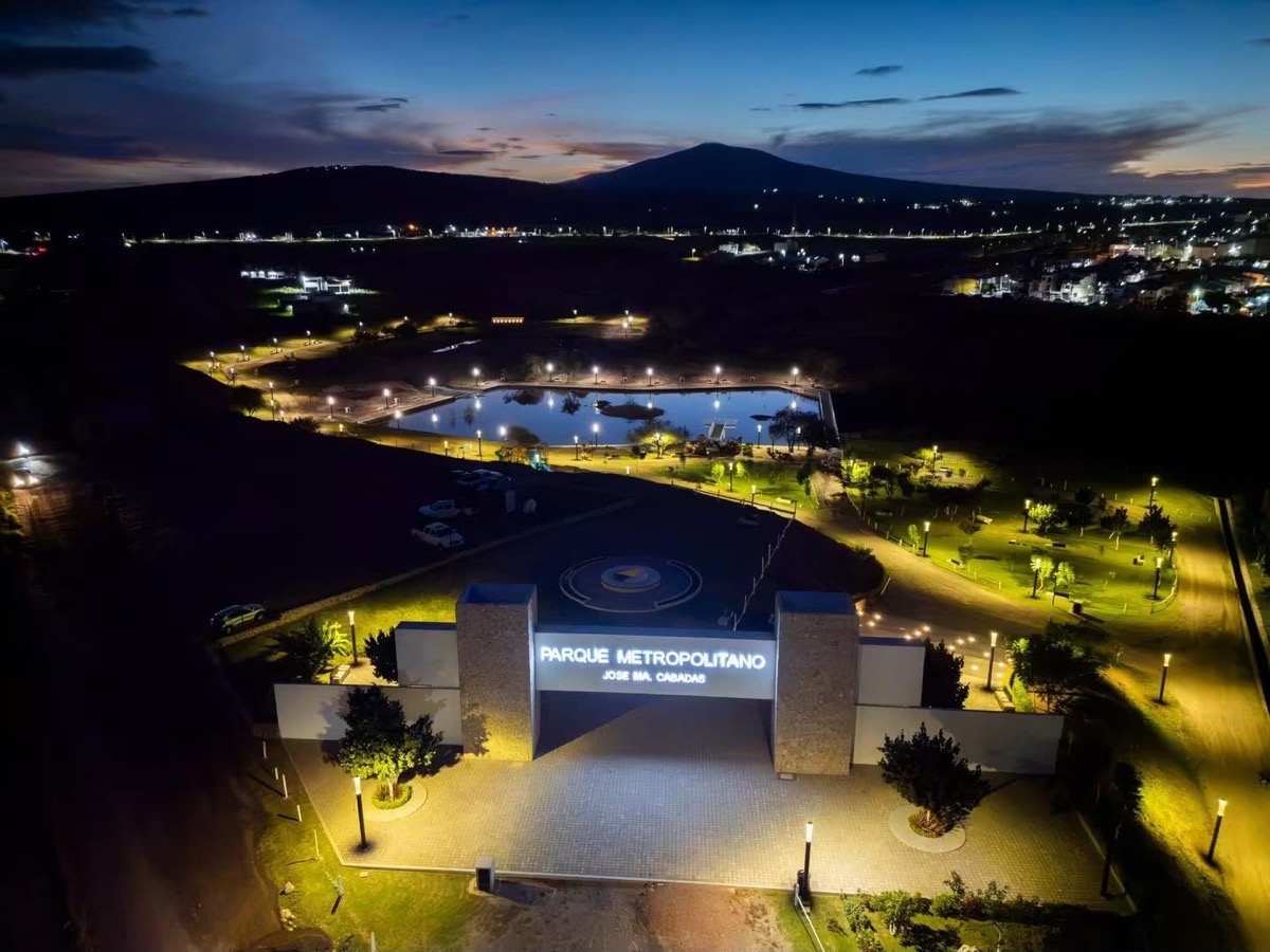 Vista nocturna del Parque Metropolitano José Ma. Cabadas iluminado con lago y senderos.