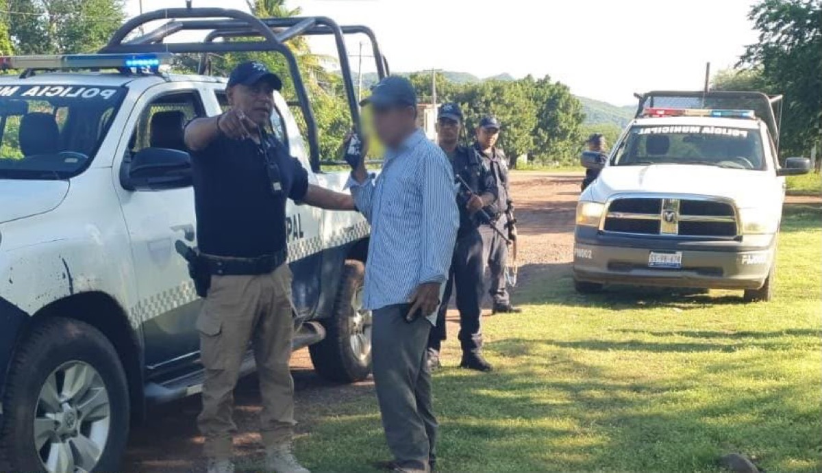 Un grupo de policías junto a patrullas detiene a un hombre en un área al aire libre.
